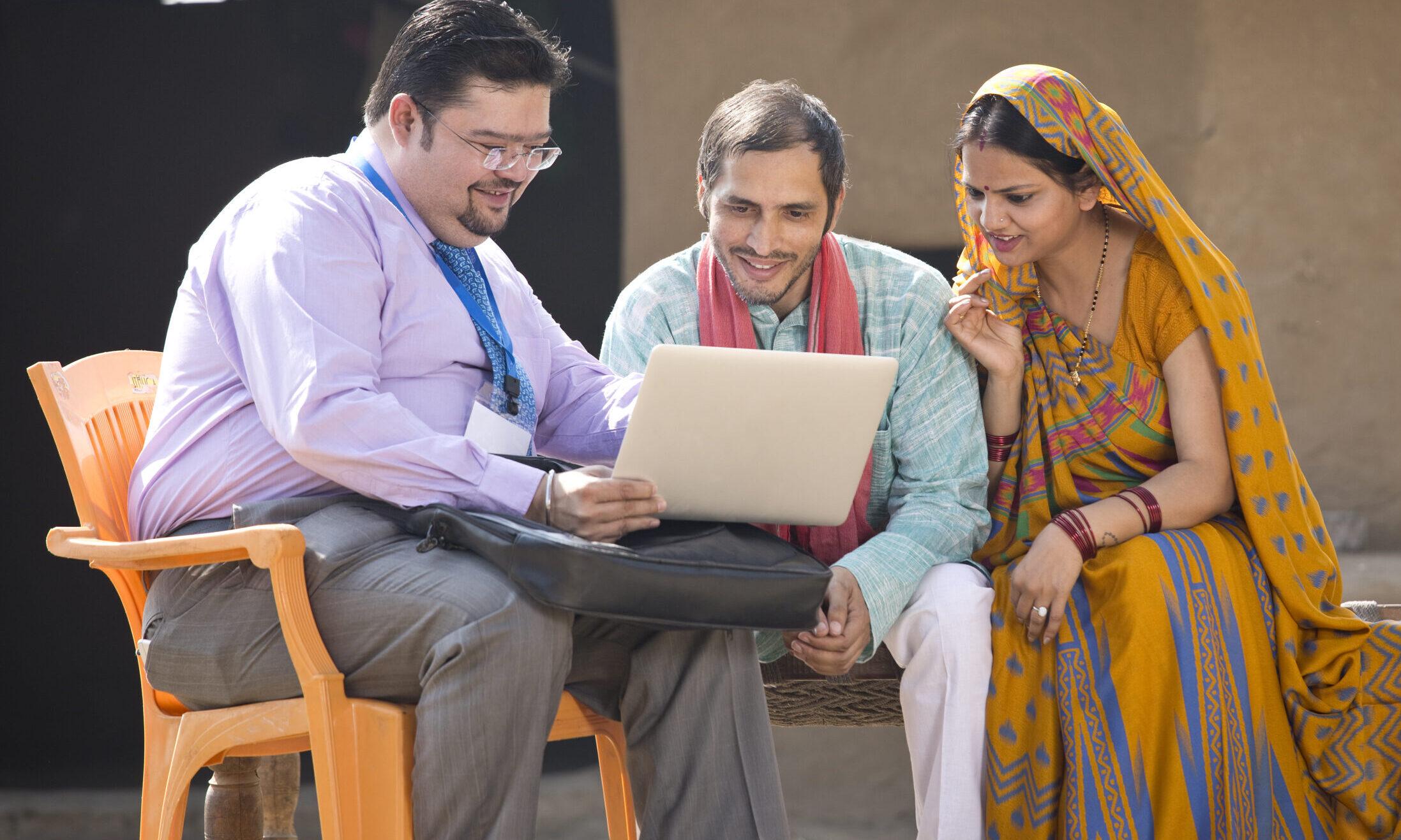 Real estate agent showing online content on laptop to rural Indian family